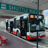 Autobus wahadłowy na **bari lotnisko** czeka na pasażerów pod znakiem "SHUTTLE BUS". Czerwona ławka stoi obok.