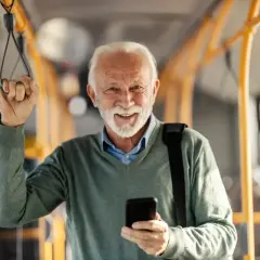 Uśmiechnięty emeryt w autobusie FlixBus, korzystający z telefonu. Sprawdza, czy ma flixbus zniżki dla emerytów na podróż.