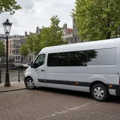 Biały bus czeka na załadunek, gotowy do transportu rzeczy z adresu pod adres. W tle kanał i kamienice Amsterdamu.