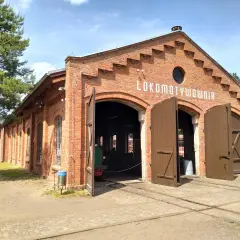 Historyczna lokomotywownia w Raciborzu, ceglany budynek z otwartymi wrotami, zaprasza do zwiedzania.