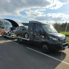 Laweta z autami pod nowoczesnym budynkiem, jak dojadę rzeszów? Słońce i chmury na niebie.