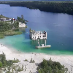 Estonia krajobrazy: zatopiony budynek w turkusowej wodzie, plaża z ludźmi, otoczone lasem.