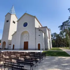 Nowy kościół w Loretto, z wieżą i kamienną fasadą, otoczony drzewami. Miejsce pielgrzymek do Matki Boskiej Loretanskiej.