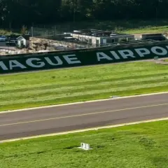 The Hague Airport z wielkimi białymi literami na zielonym tle. Pas startowy i budynki lotniska.