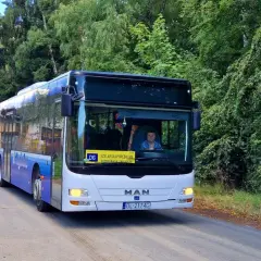 Autobus linii D6 z napisem "SZKLARSKA PORĘBA GRN" jedzie drogą wśród zieleni.