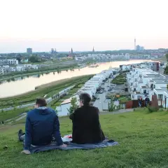 Dwa osoby siedzą na trawie, podziwiając panoramę nowoczesnego osiedla nad wodą w Dortmundzie.