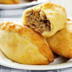Złociste pierogi litewskie z mięsnym farszem, jeden przekrojony, ukazujący soczyste wnętrze.