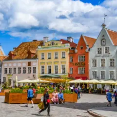 Tętniący życiem plac w Tallinnie, stolicy Estonii, z kolorowymi kamieniczkami i ludźmi odpoczywającymi w kawiarnianych ogródkach.