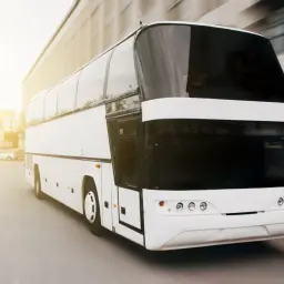 Biały, nowoczesny omnibus pędzi ulicą w słoneczny dzień.