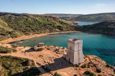 Kamienna wieża strażnicza nad zatoką z piaszczystą plażą, przypominającą widok z Bugibba Beach.