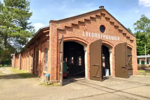 Historyczna lokomotywownia w Raciborzu, ceglany budynek z otwartymi wrotami, zaprasza do zwiedzania.