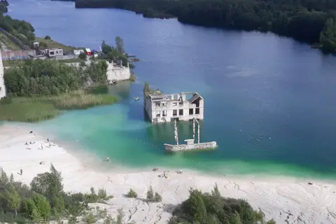 Estonia krajobrazy: zatopiony budynek w turkusowej wodzie, plaża z ludźmi, otoczone lasem.