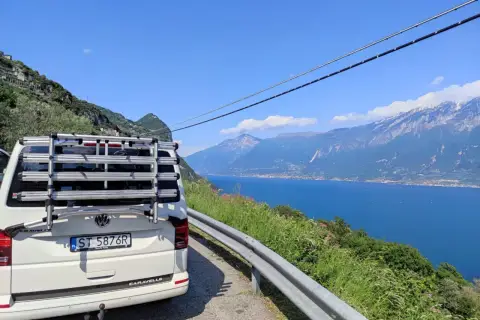 Biały bus z bagażnikiem na rowery na tle jeziora i gór we Włoszech. Czas podróży autokarem do Włoch zależy od trasy.