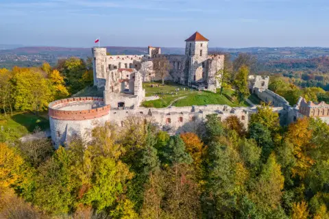 Ruiny zamku na wzgórzu, otoczone jesiennym lasem. Ta malownicza lokacja zachwyca o każdej porze roku.