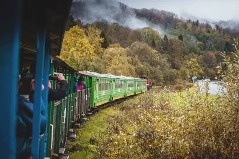 Zielony pociąg turystyczny mknie przez jesienne Bieszczady, zabierając pasażerów z Krakowa na malowniczą podróż.