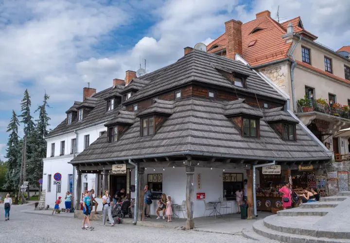 Urokliwy rynek w Kazimierzu Dolnym i okolice. Ludzie spacerują, kupują lody i gofry pod drewnianymi dachami.