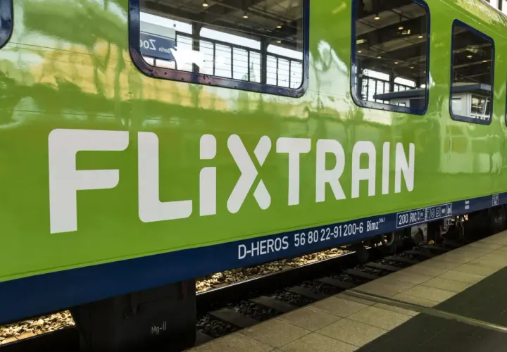 Zielony pociąg FlixTrain z białym logo na tle torów kolejowych.