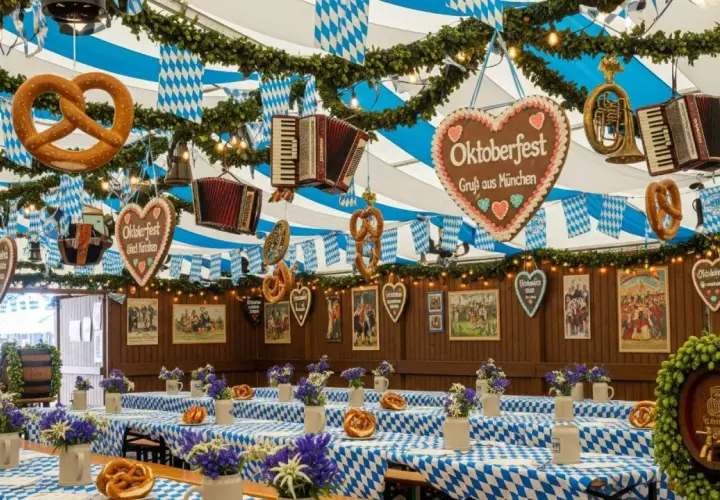 Wnętrze namiotu udekorowane na Oktoberfest. Wiszące precle, serca z napisem "Oktoberfest" i akordeony. Stoły przykryte niebiesko-białymi obrusami.