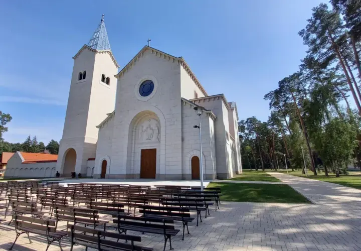 Nowy kościół w Loretto, z wieżą i kamienną fasadą, otoczony drzewami. Miejsce pielgrzymek do Matki Boskiej Loretanskiej.