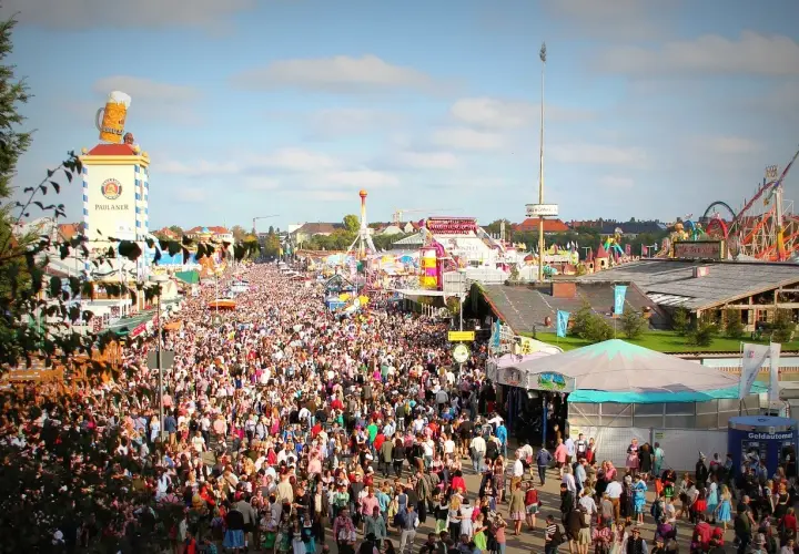 Tłum ludzi na festynie, widoczny wieżowiec z wielkim kuflem piwa i karuzele. To prawdziwy Oktoberfest!