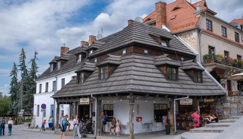Urokliwy rynek w Kazimierzu Dolnym i okolice. Ludzie spacerują, kupują lody i gofry pod drewnianymi dachami.