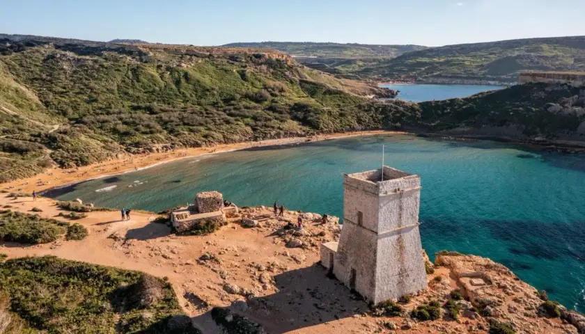 Kamienna wieża strażnicza nad zatoką z piaszczystą plażą, przypominającą widok z Bugibba Beach.