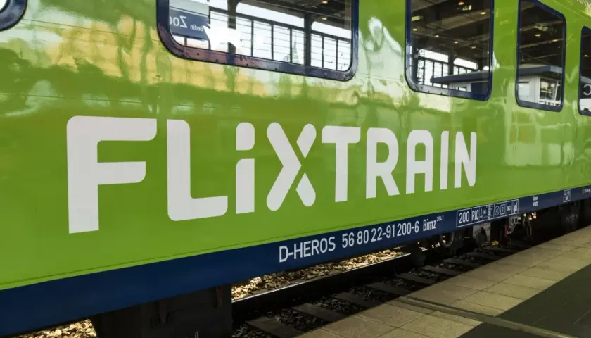 Zielony pociąg FlixTrain z białym logo na tle torów kolejowych.