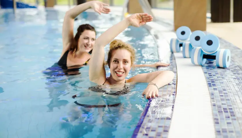 Dwie kobiety ćwiczą w basenie. Obok leżą hantle do aquafitness. Sprawdź nasz primavera basen cennik!