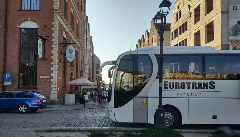 Autobusy do Chorwacji czekają na pasażerów przy brukowanej ulicy, obok ceglanych kamienic.