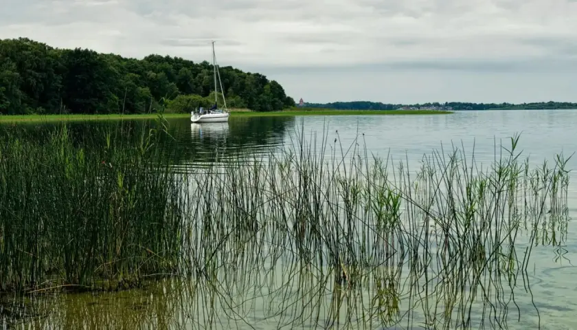 Żaglówka na jeziorze, w oddali las i zabudowania. Odległość do Mikołajek Giżycko.