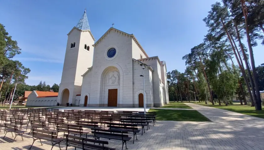 Nowy kościół w Loretto, z wieżą i kamienną fasadą, otoczony drzewami. Miejsce pielgrzymek do Matki Boskiej Loretanskiej.