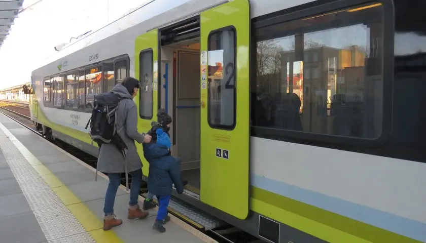 Matka z dzieckiem wsiada do pociągu na stacji Bydgoszcz. Zielona góra na pociągu symbolizuje ekologiczny transport.