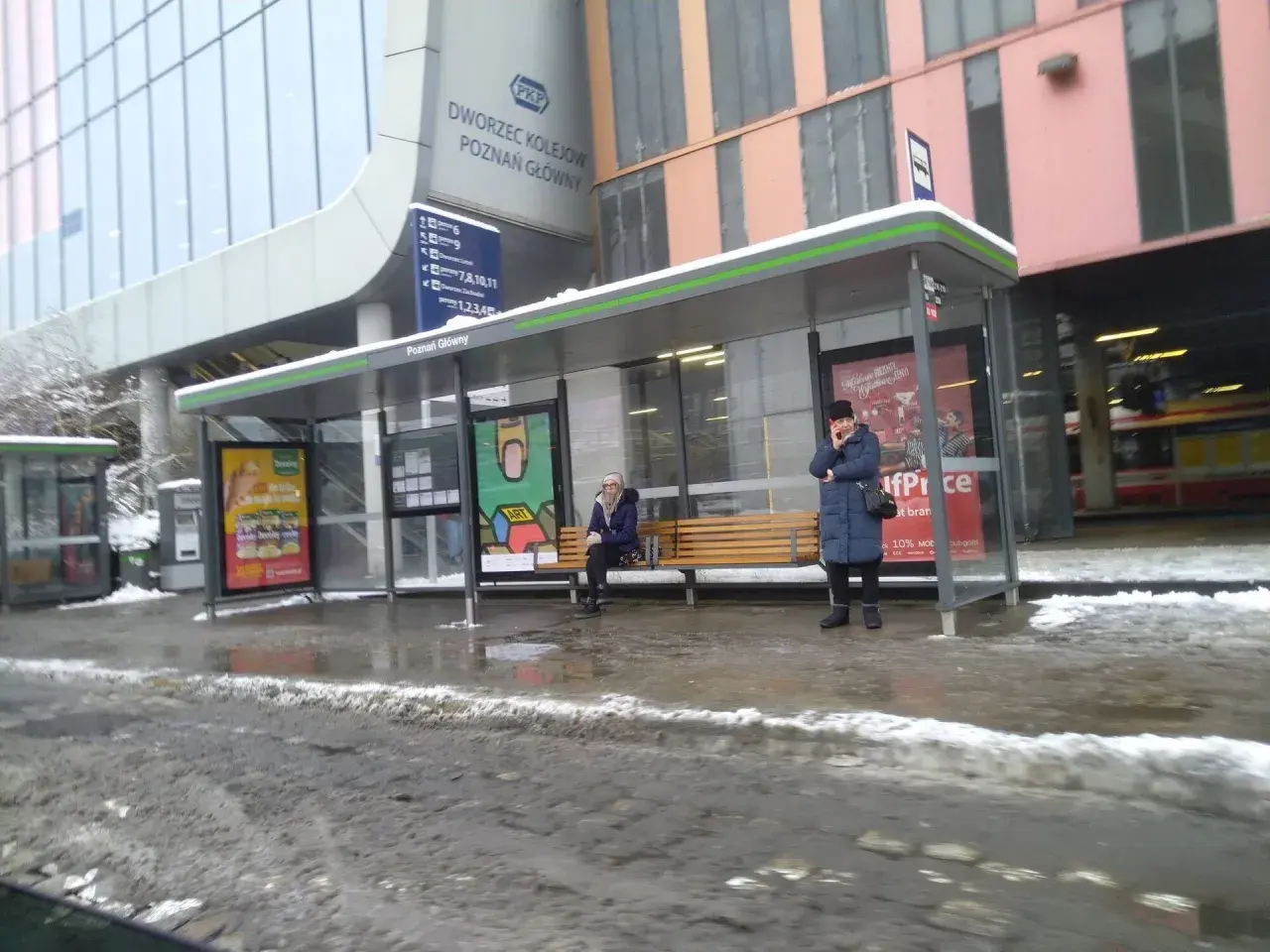 Z dworca PKP Poznań Główny na lotnisko dojedziesz autobusem. Na przystanku czekają pasażerowie.