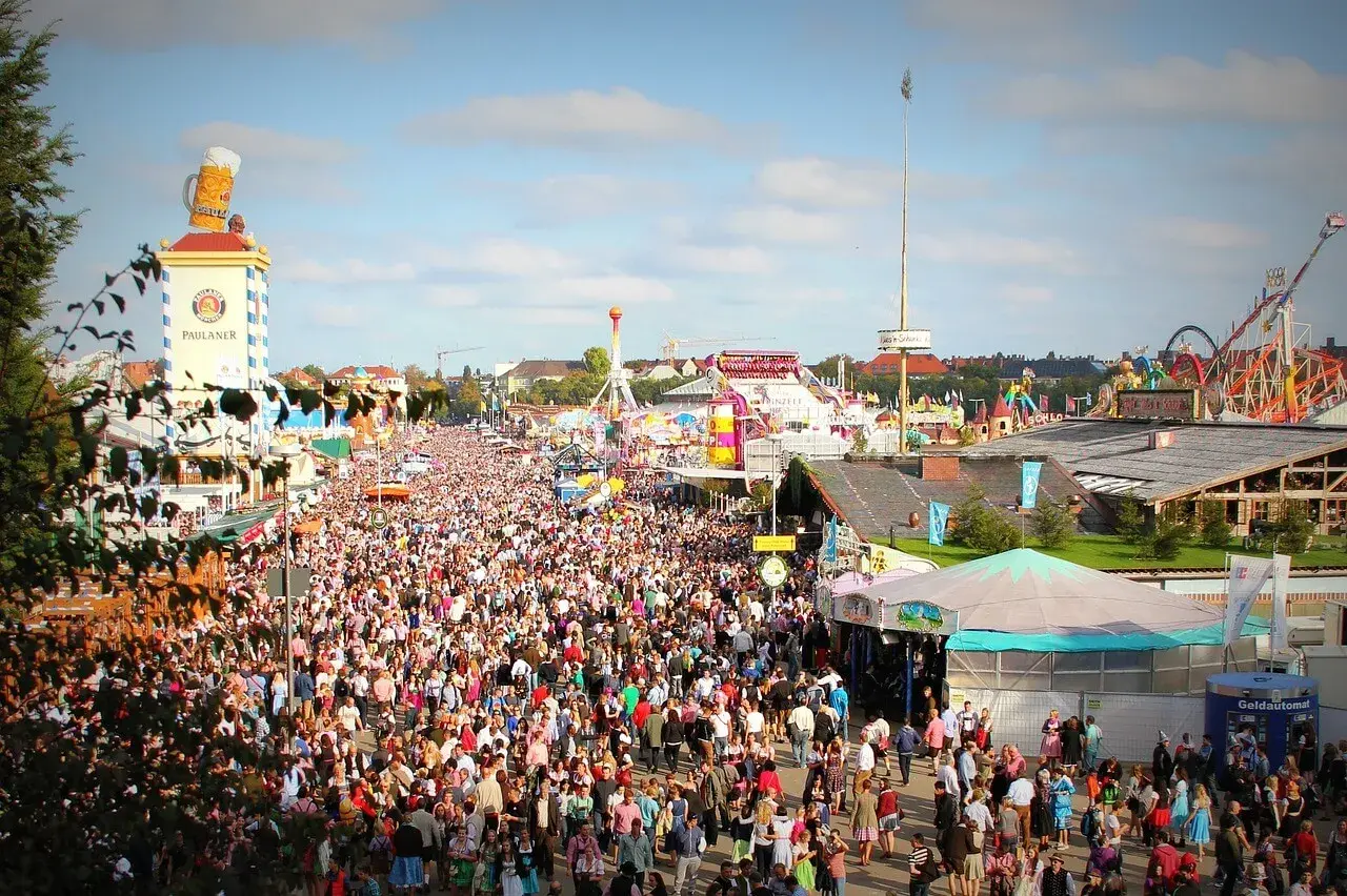 Tłum ludzi na festynie, widoczny wieżowiec z wielkim kuflem piwa i karuzele. To prawdziwy Oktoberfest!