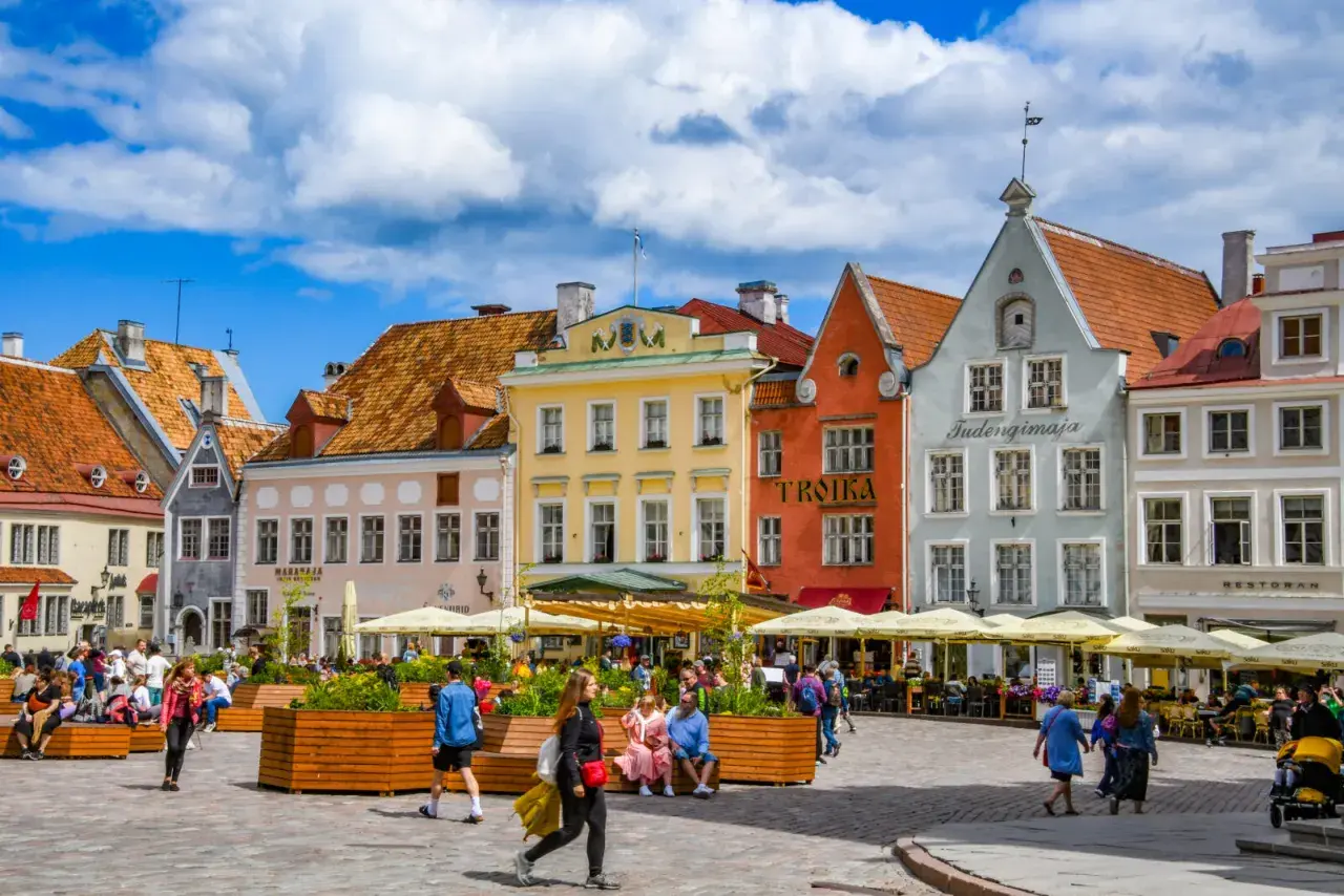 Tętniący życiem plac w Tallinnie, stolicy Estonii, z kolorowymi kamieniczkami i ludźmi odpoczywającymi w kawiarnianych ogródkach.