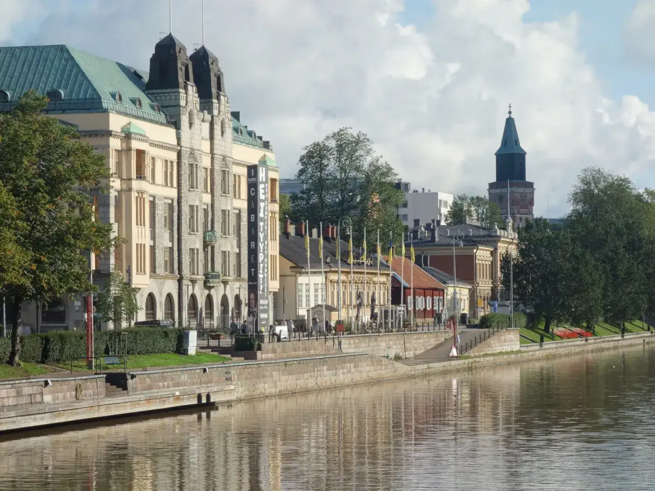 Nad rzeką w Turku, najstarszym mieście w Finlandii, stoją zabytkowe budynki z charakterystyczną wieżą kościelną w tle.