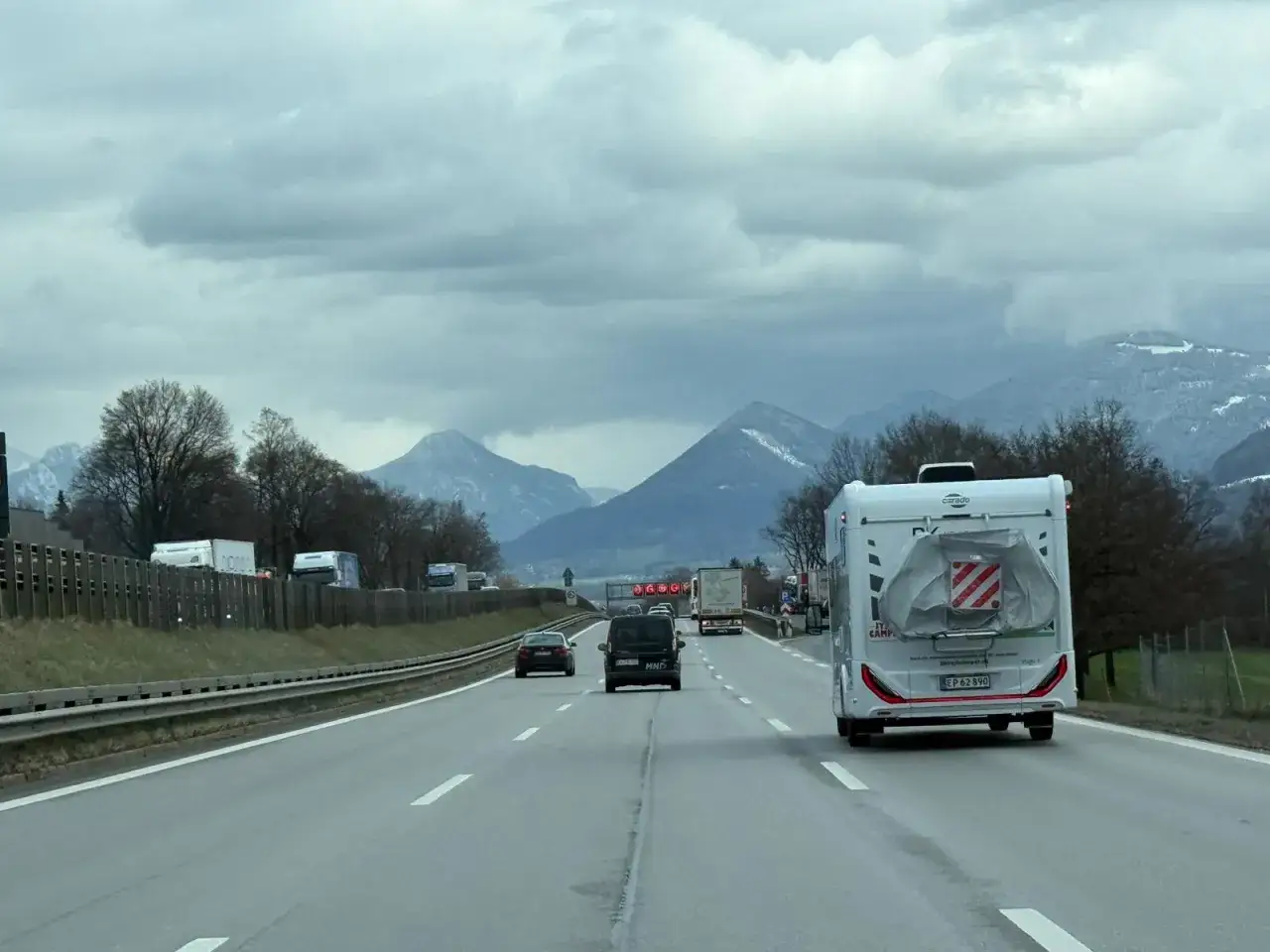 Autostradą do Włoch, z kamperem na czele. Góry w tle, chmury na niebie.