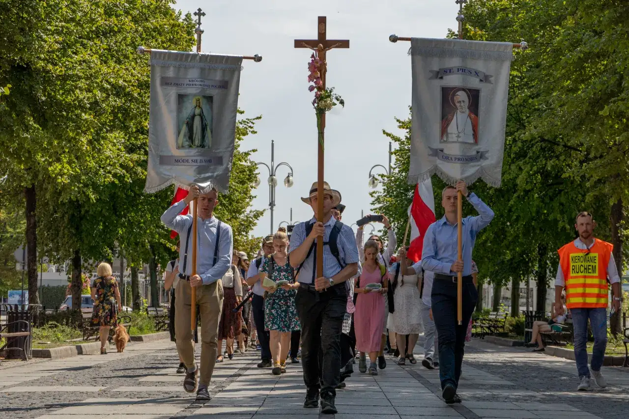 Uczestnicy peregrynacji niosą krzyż i sztandary z wizerunkami Matki Bożej i św. Piusa X.