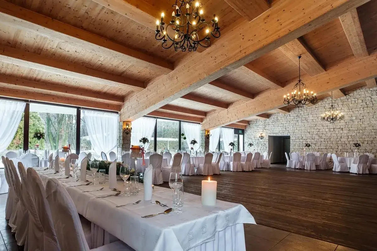Elegancka sala bankietowa z drewnianym sufitem i kamienną ścianą, idealna na wesele w stylu ojcowski dworek.
