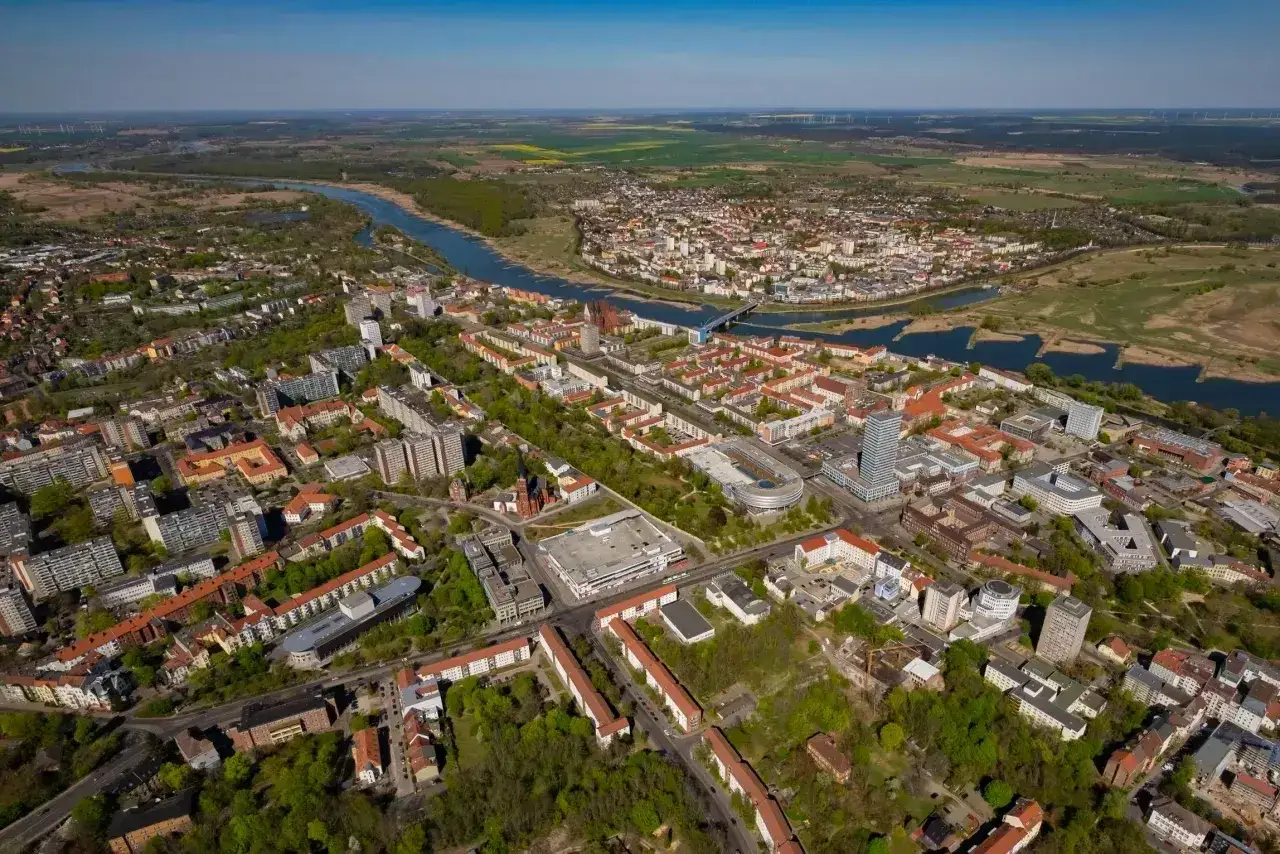 Widok z lotu ptaka na miasto nad rzeką, z nowoczesnymi budynkami i terenami zielonymi. To właśnie tutaj jest Frankfurt nad Odrą.