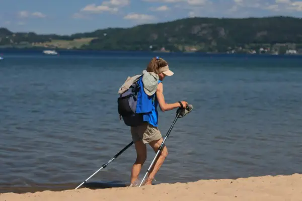 Osoba z plecakiem i kijkami do nordic walking nad morzem, wchodząca do wody.